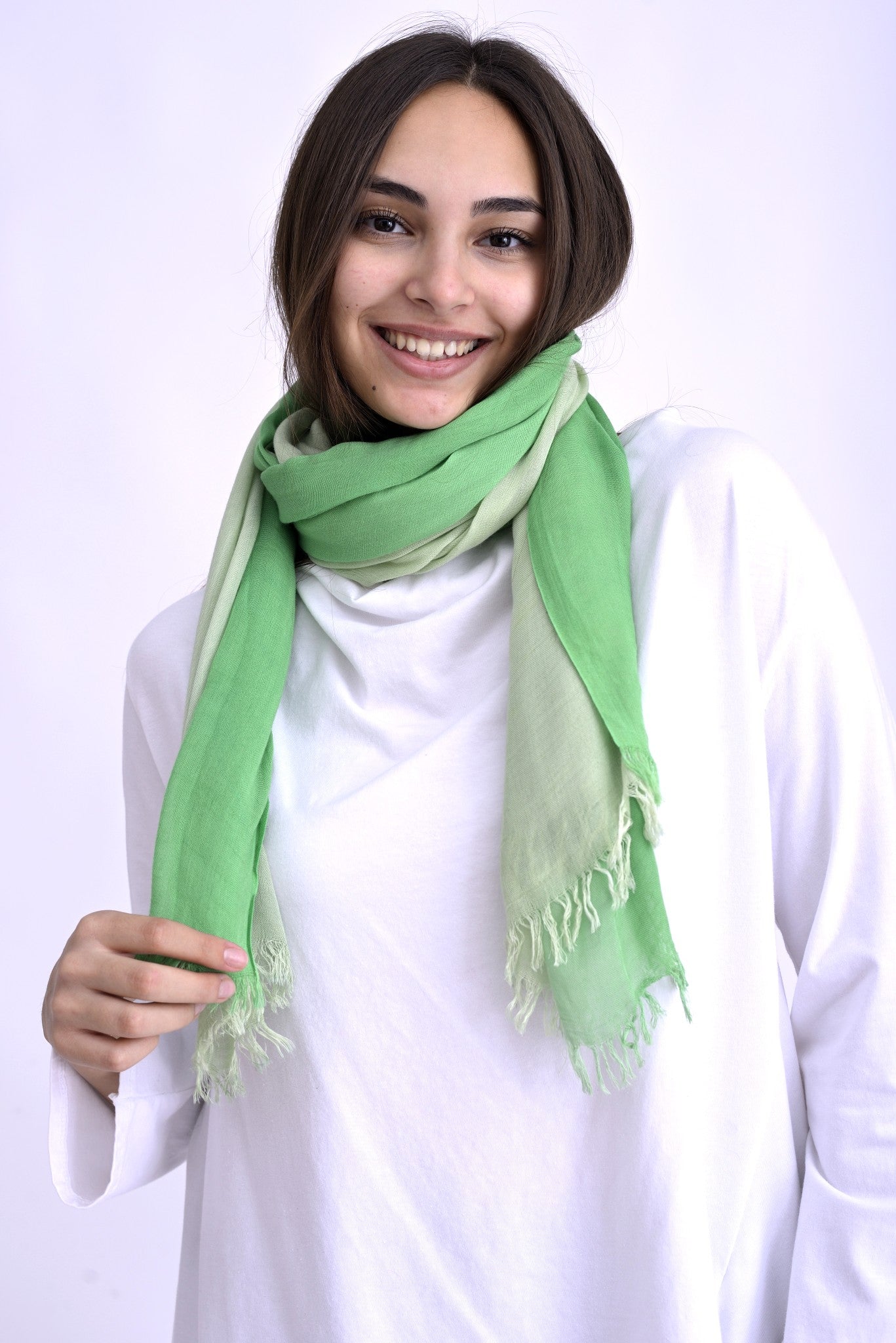 Model purtând o eșarfă verde în degrade, cu nuanțe deschise și închise, asortată la o bluză albă cu mâneci lungi.