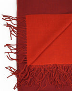 Gros-plan pe franjurii fini ai fularului pashmina roșu, material texturat și dens.