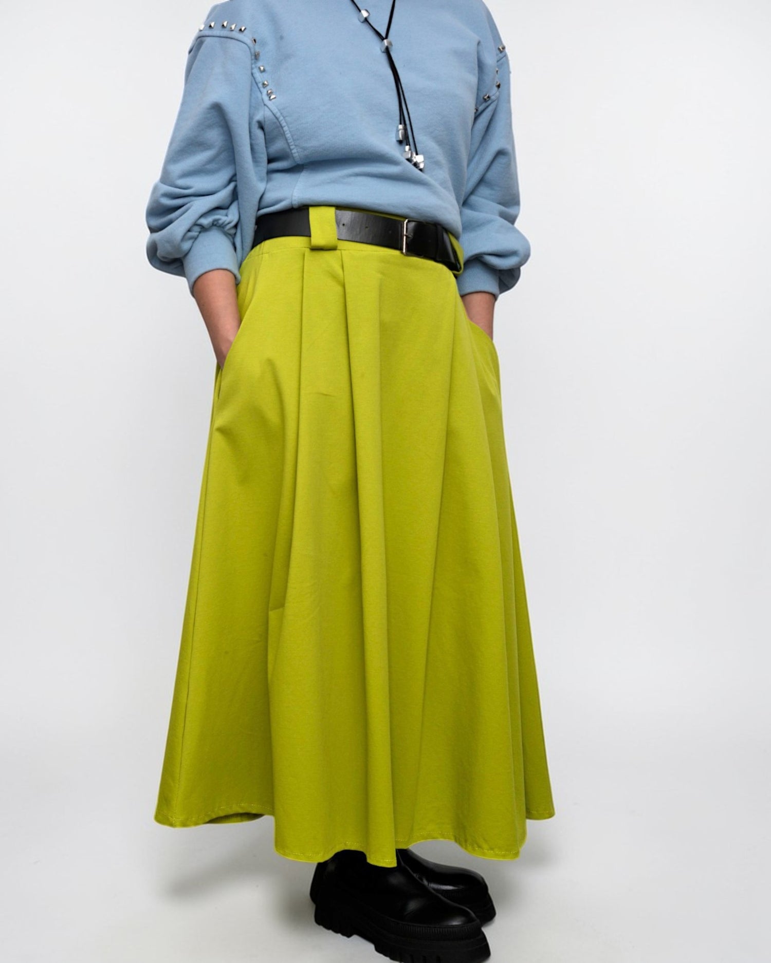 Model purtând o fustă midi cu pliuri largi și curea neagră.