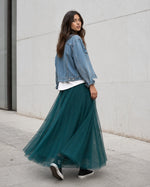 Model poartă fustă lungă din tul turcoaz cu bandă satinată, tricou alb lejer, jachetă scurtă din denim și teniși Converse.