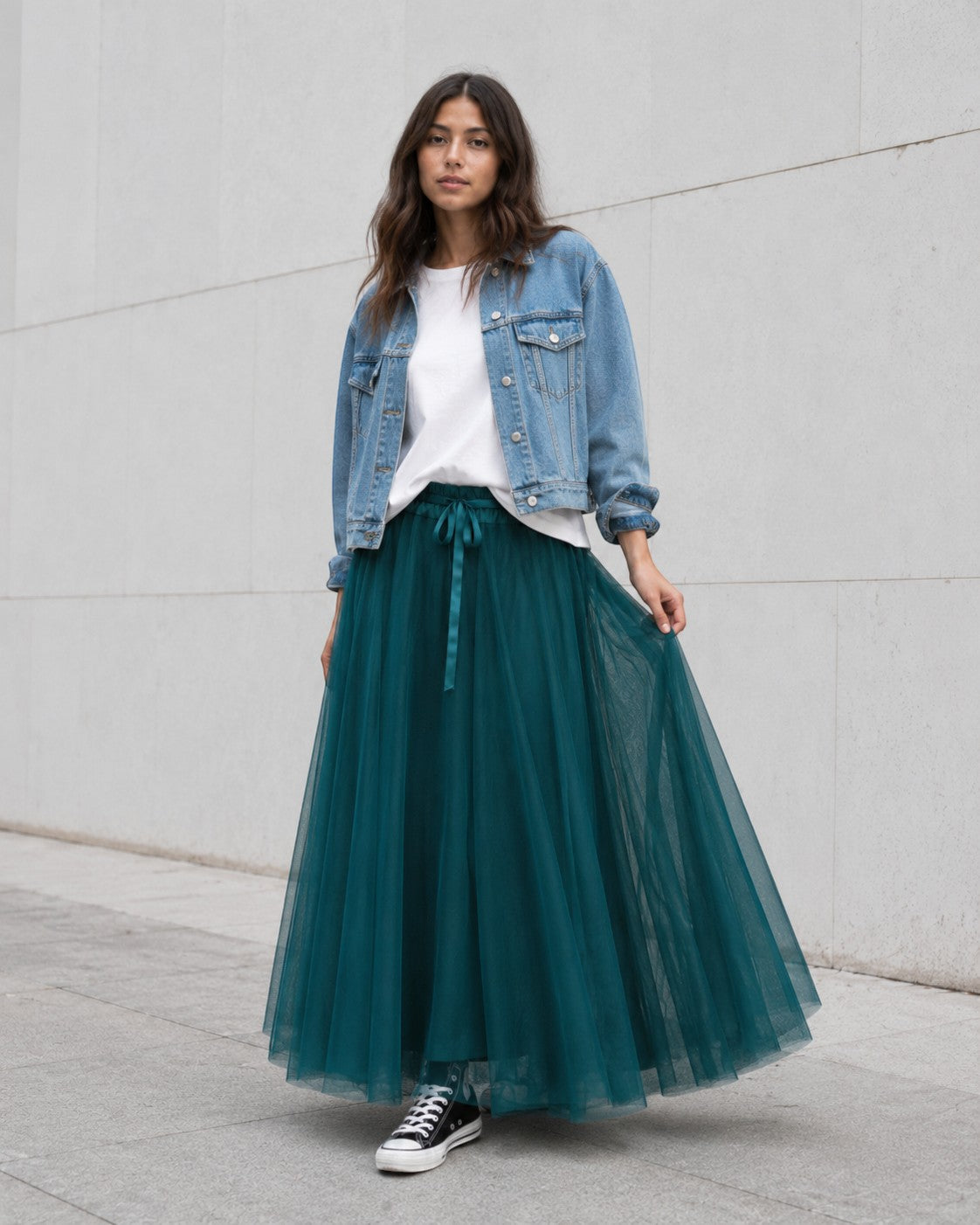 Model poartă fustă lungă din tul turcoaz cu bandă satinată, tricou alb lejer, jachetă scurtă din denim și teniși Converse.