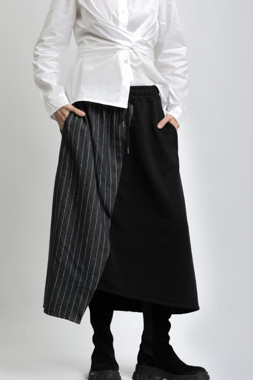 Fustă asimetrică din jerse negru cu panou cu imitație de jeans, purtată cu cămașă albă și bocanci.