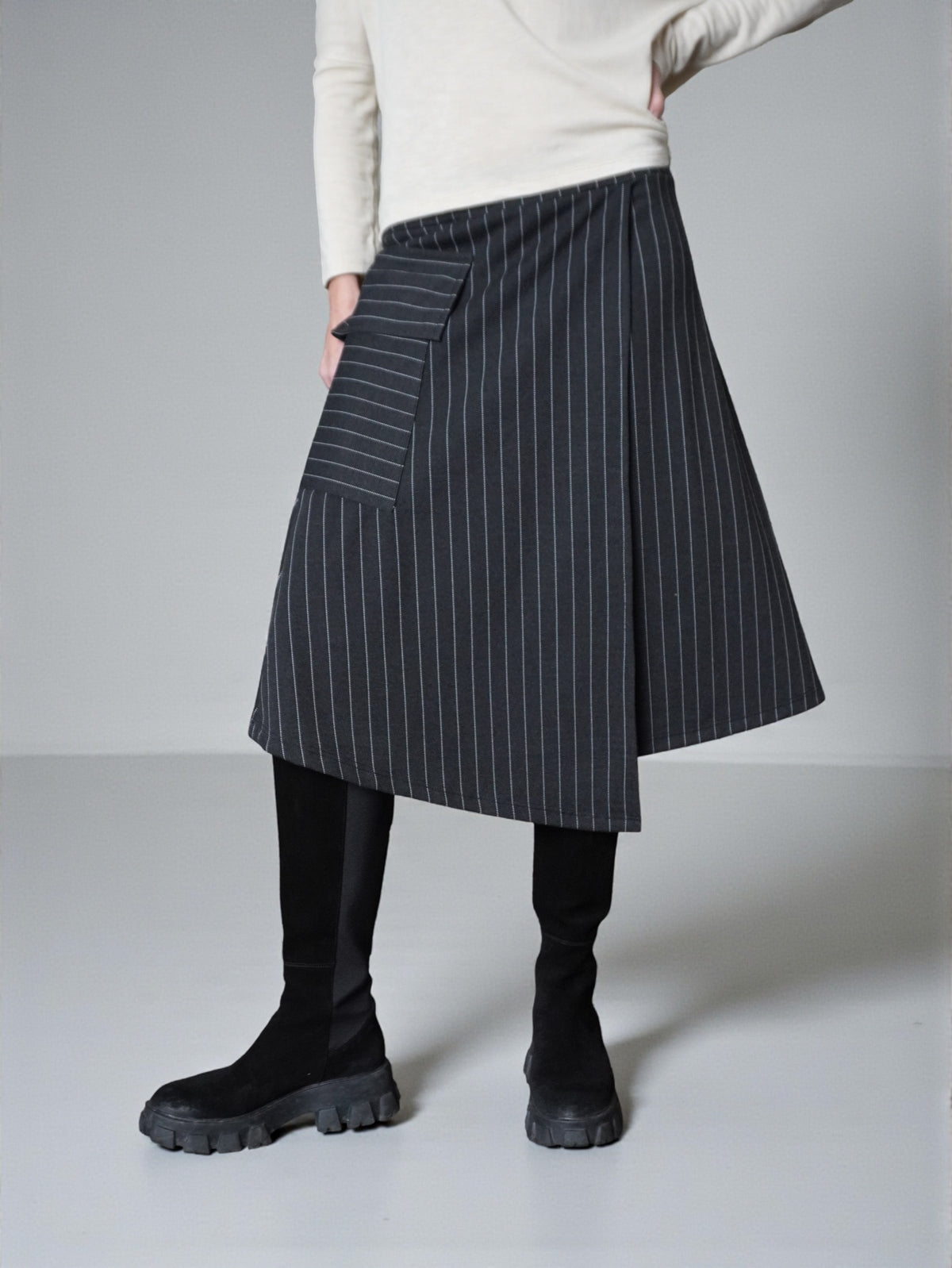 Fustă în dungi cu suprapunere frontală, surprinsă în mișcare, evidențiind fluiditatea materialului.