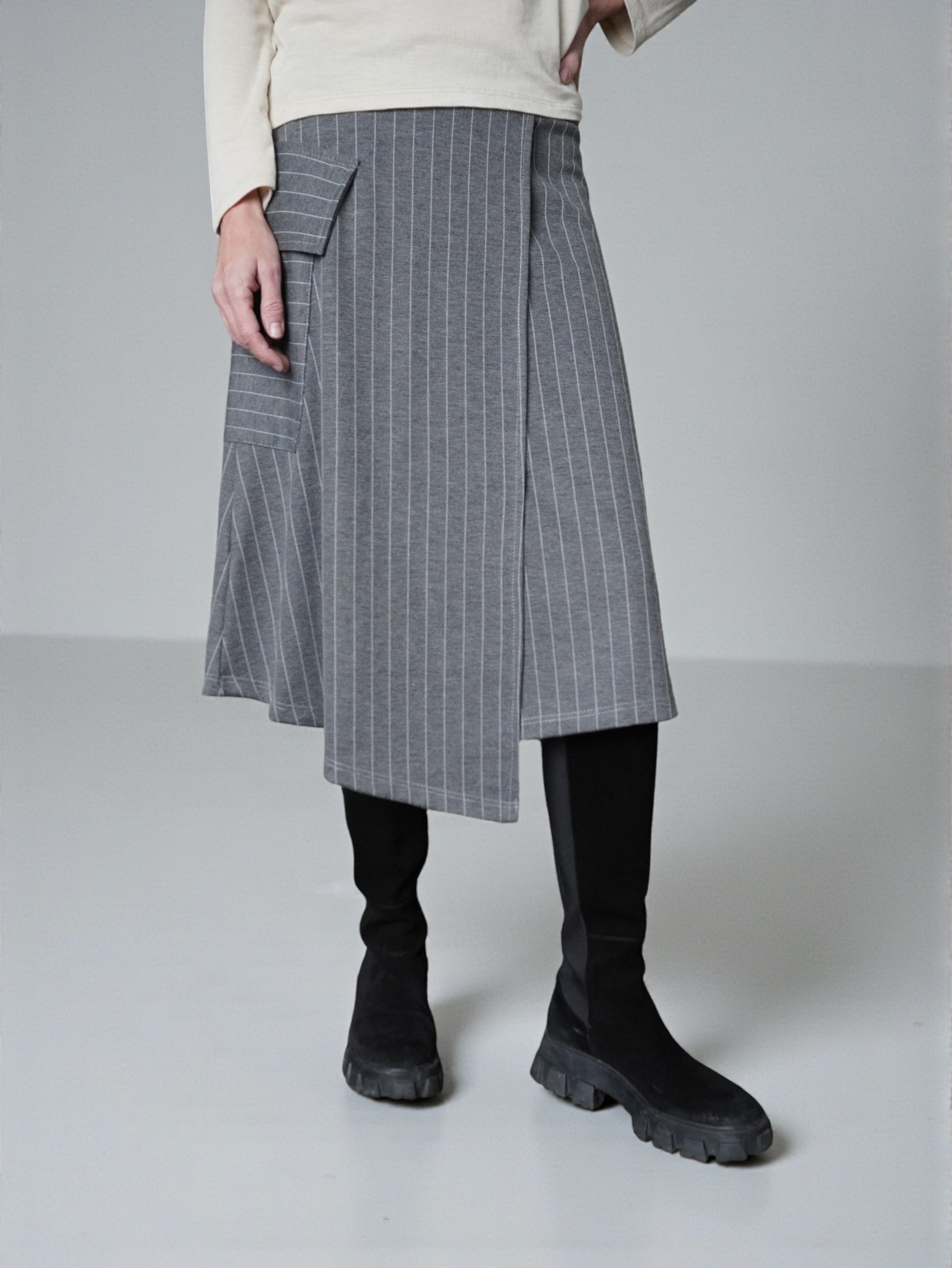 Fustă midi în dungi fine, cu colț suprapus și croială asimetrică, purtată cu cizme negre.