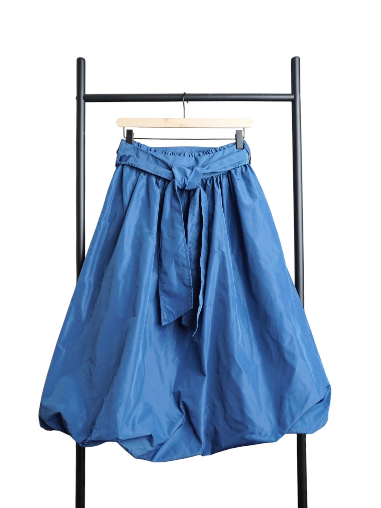 Fustă albastru cu croială gogoșar și fundă laterală decorativă, realizată din material ușor și lucios, stil casual-modern