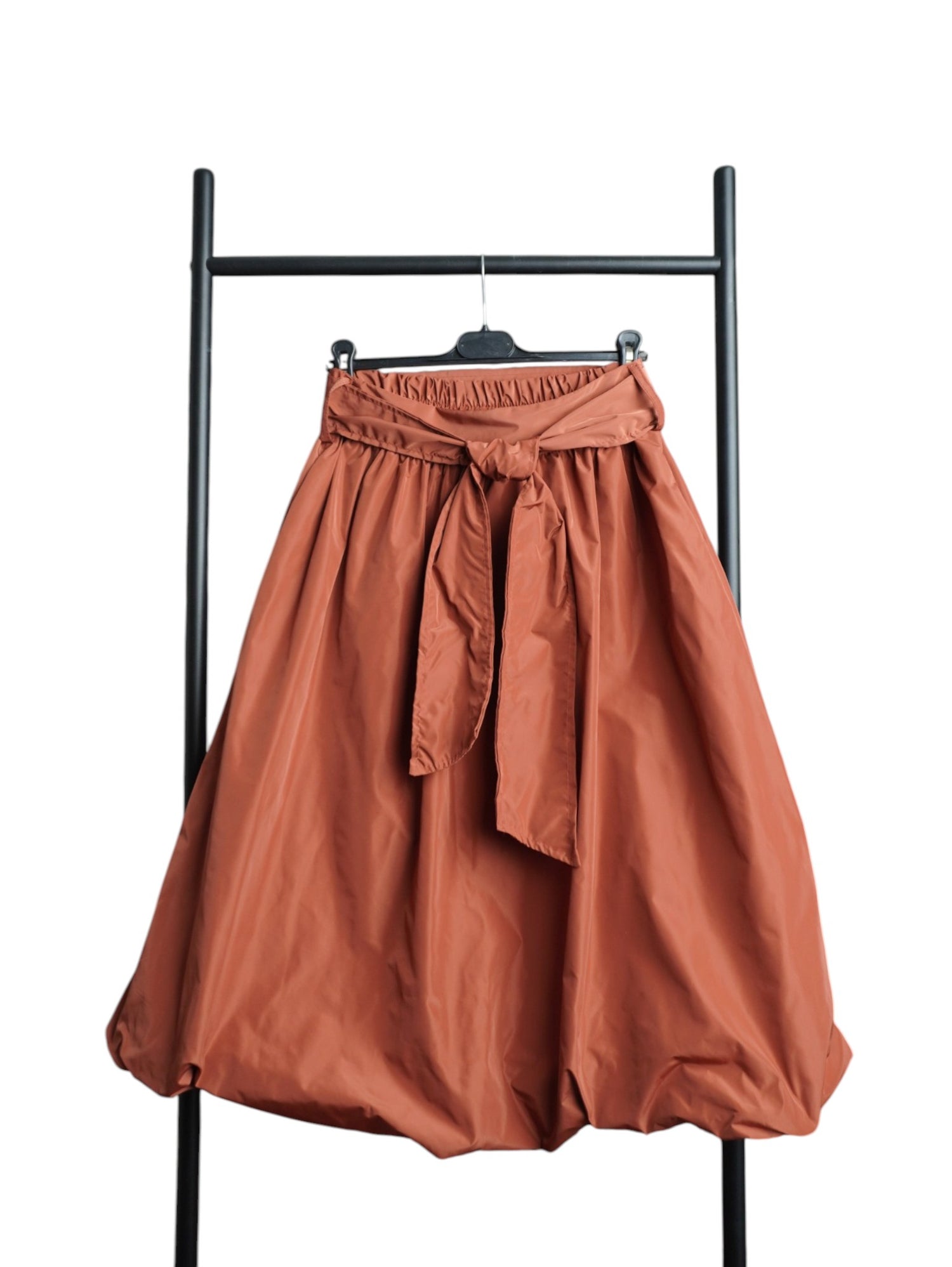 Fustă portocaliu inchis cu croială gogoșar și fundă laterală decorativă, realizată din material ușor și lucios, stil casual-modern