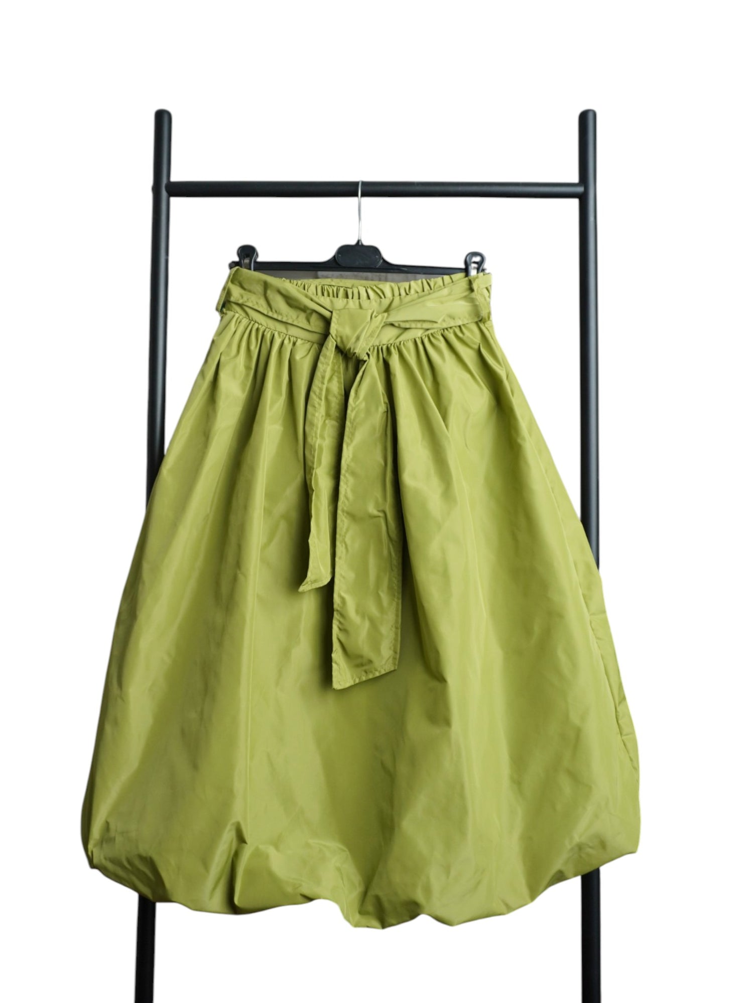 Fustă verde cu croială gogoșar și fundă laterală decorativă, realizată din material ușor și lucios, stil casual-modern