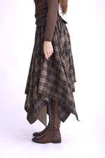 Detaliu de material al fustei în colțuri, țesătură texturată cu model în carouri, tonuri de maro, gri și negru.