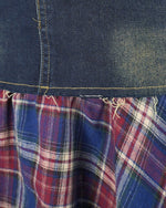 Detaliu cusături și material din denim albastru combinat cu inserții carouri.