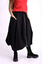 Fustă neagră cu material fluid, cădere amplă și detaliu de fermoar poziționat asimetric.