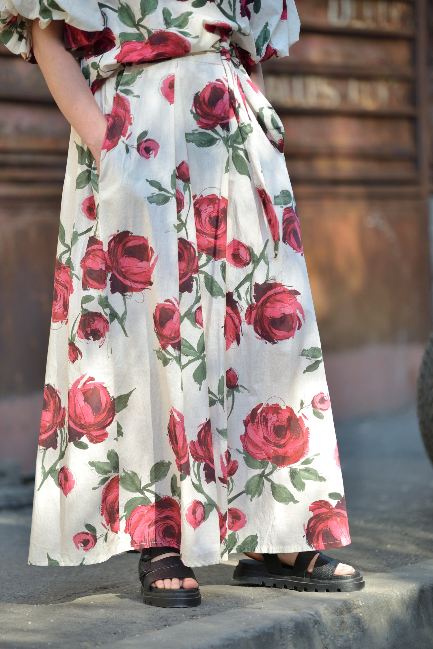 Fustă lungă albă cu imprimeu floral și pliseuri în talie, văzută din față, purtată casual.