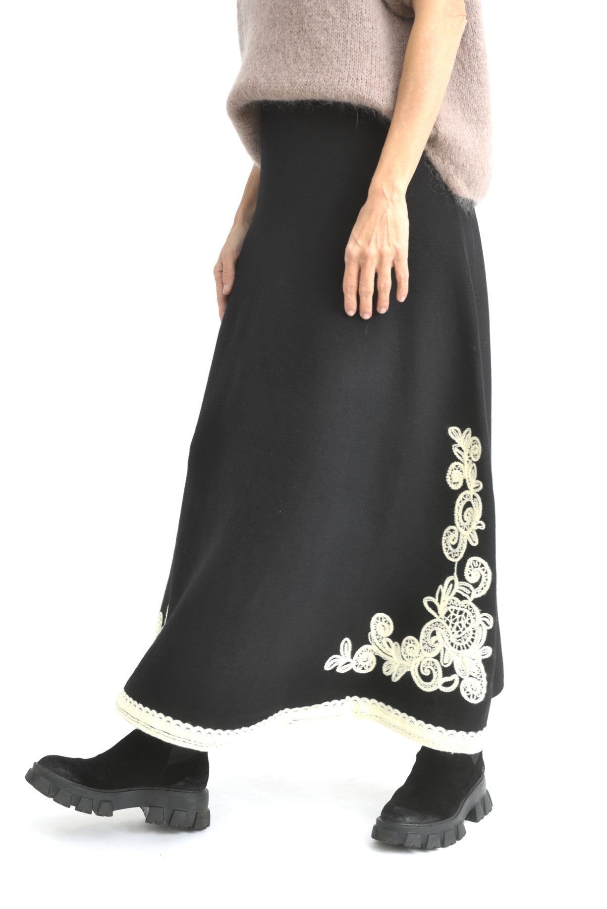 Vedere din spate a fustei crem din tricot, lungă și fluidă, cu broderie contrastantă pe margine.