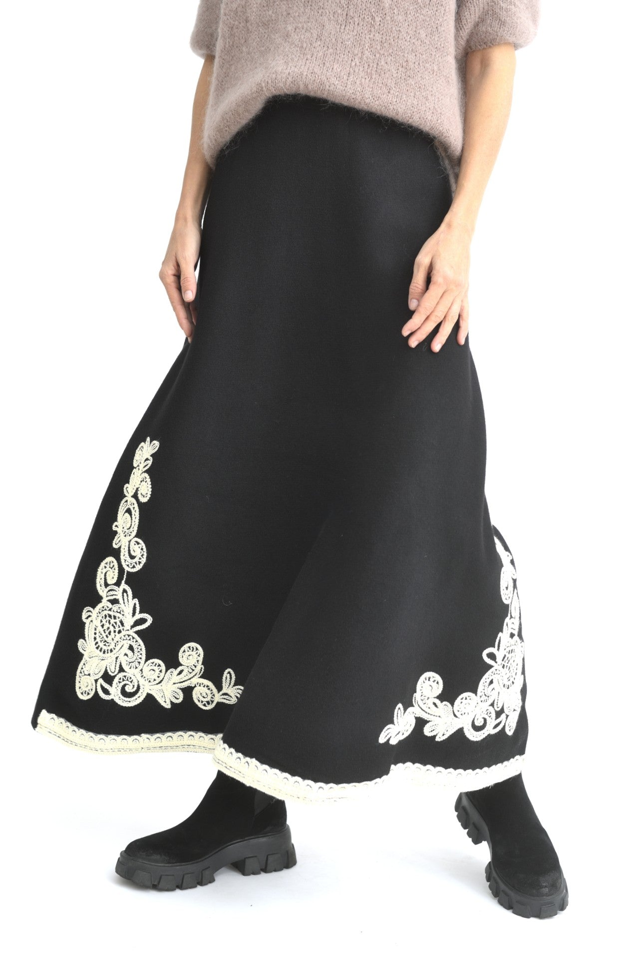 Fustă lungă evazată din tricot negru, cu broderie contrastantă albă în partea de jos, purtată cu pulover lejer și bocanci.