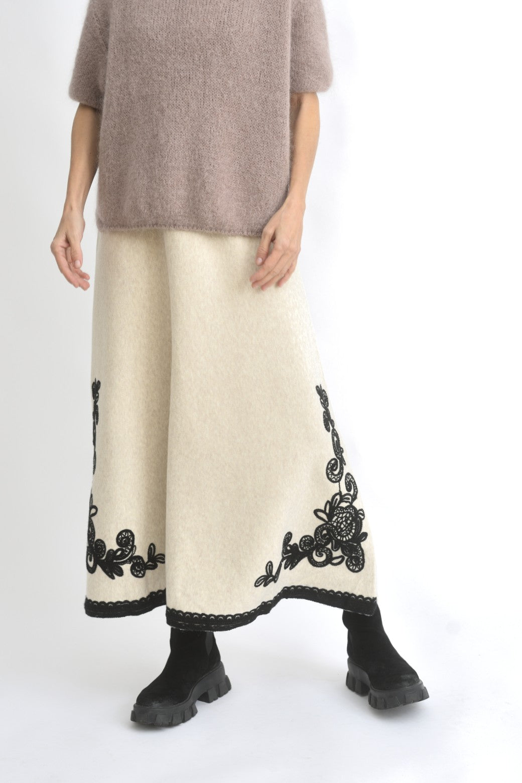 Vedere laterală a fustei lungi negre din tricot, cu croială evazată și broderie decorativă pe tiv.