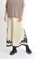 Vedere laterală a fustei lungi negre din tricot, cu croială evazată și broderie decorativă pe tiv.