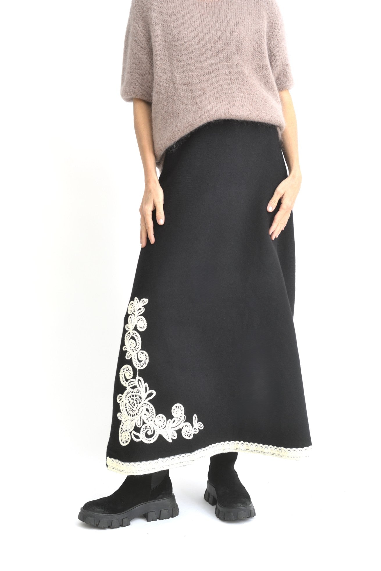 Fustă neagră din tricot văzută din spate, lungă până la gleznă, cu tiv brodat contrastant.