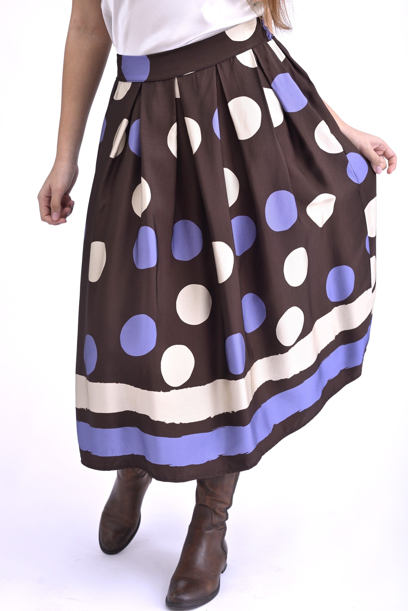 Model purtând o fustă midi bleumarin cu buline albe și maro, stilizată cu top satinat gri închis și cizme maro, pentru un look elegant de zi.