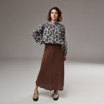 Fustă midi maro cu textură fină, purtată cu bluză florală și pantofi bej, într-un look boem elegant.