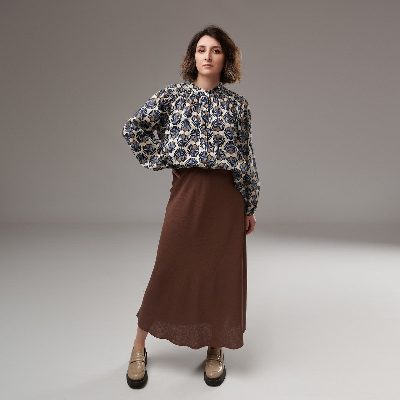 Fustă midi maro cu textură fină, purtată cu bluză florală și pantofi bej, într-un look boem elegant.