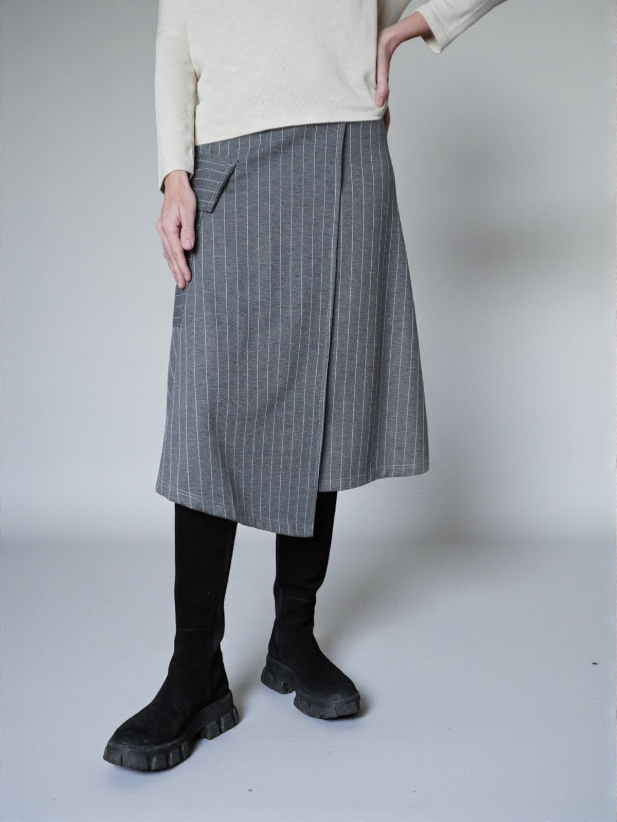 Fustă midi în dungi fine, surprinsă în mișcare, cu colț suprapus discret.