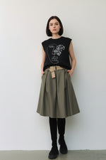 Fustă midi evazată kaki, purtată cu top negru și bocanci, evidențiind talia cu curea textilă.