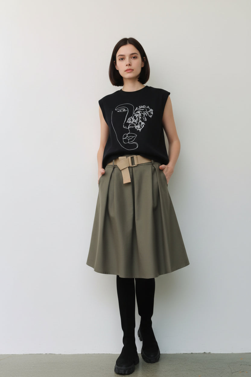 Fustă midi evazată kaki, purtată cu top negru și bocanci, evidențiind talia cu curea textilă.