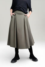 Fustă midi evazată kaki, purtată cu pulover negru și bocanci, evidențiind croiala fluidă și talia elastică.