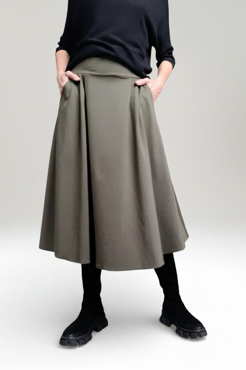 Fustă midi evazată kaki, purtată cu pulover negru și bocanci, evidențiind croiala fluidă și talia elastică.