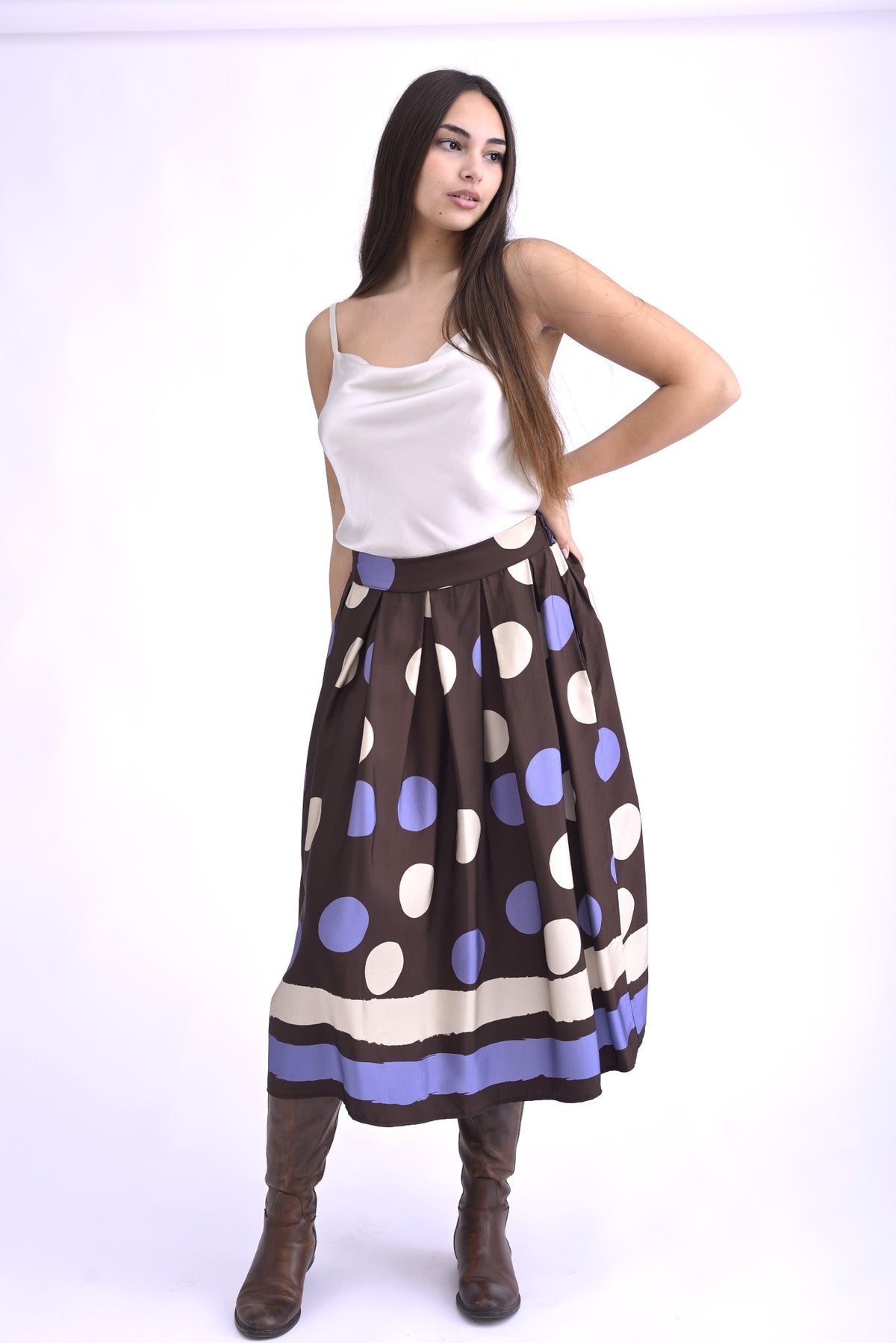 Detaliu al unei fuste midi maro cu pliuri și imprimeu cu buline mov și albe, evidențiind textura și lejeritatea materialului.