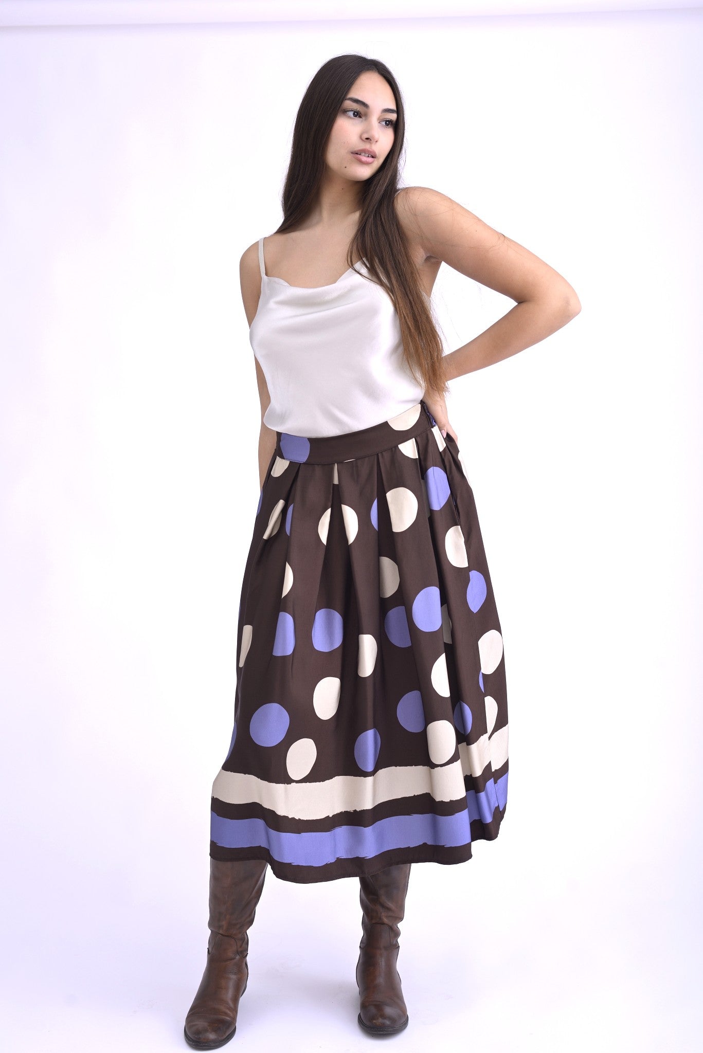 Detaliu al unei fuste midi maro cu pliuri și imprimeu cu buline mov și albe, evidențiind textura și lejeritatea materialului.