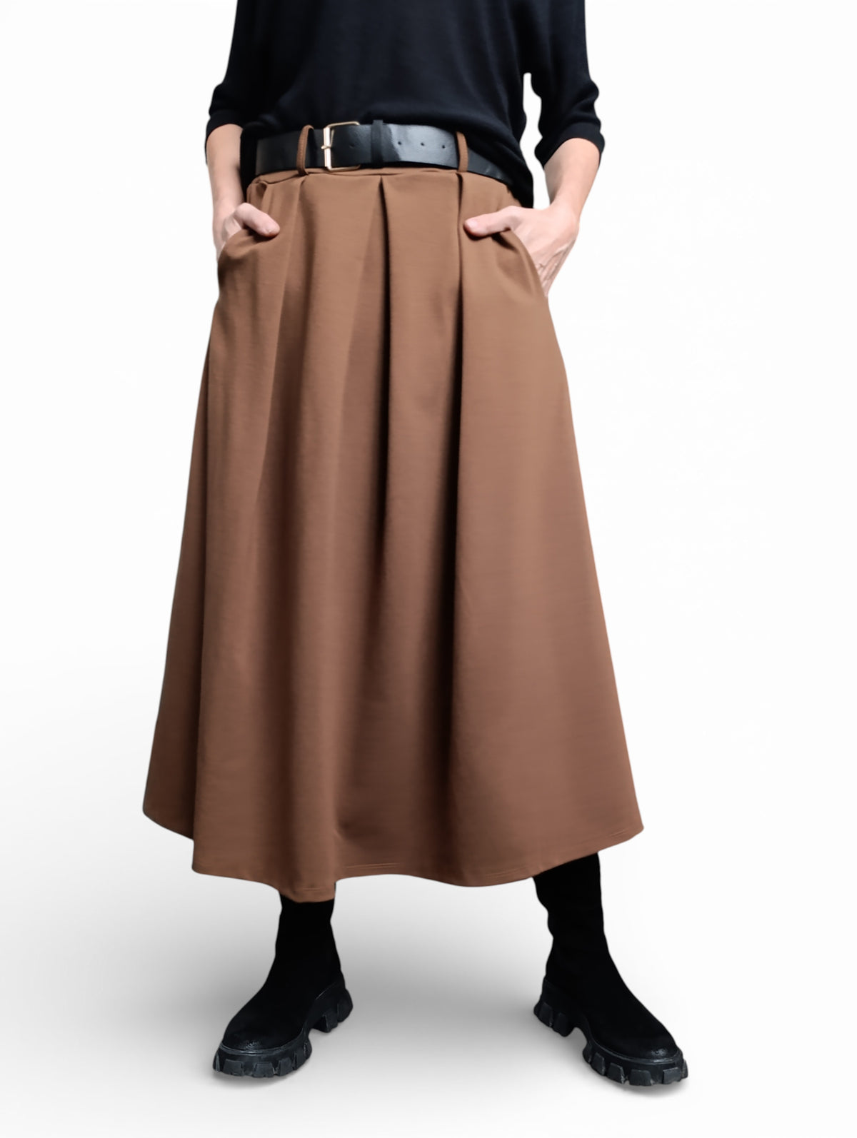 Detaliu al unei fuste maro midi cu pliuri și curea neagră, purtată cu pulover negru și cizme maro.
