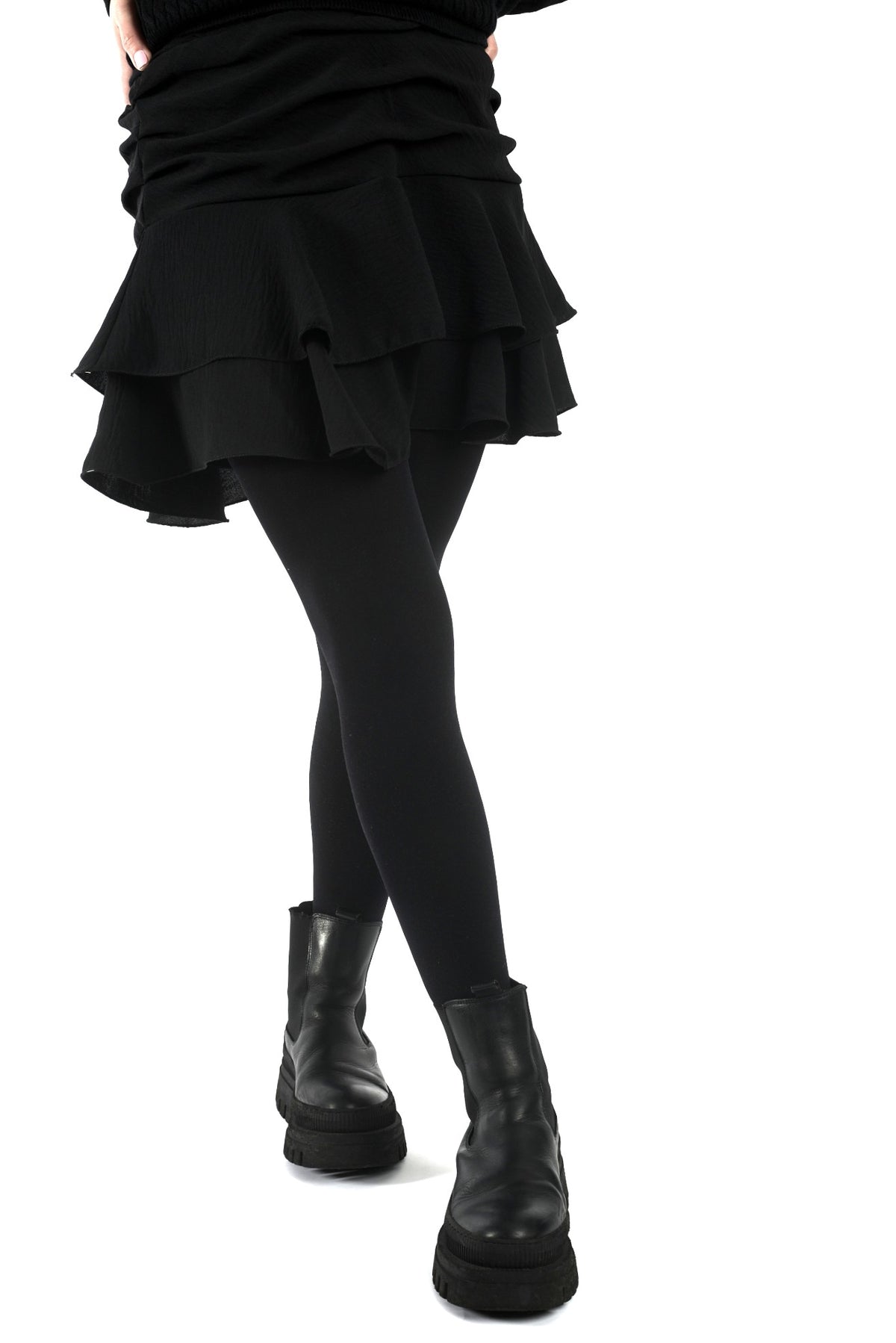 Fustă scurtă neagră cu falduri și jupă pantalon, vedere frontală, purtată cu dresuri și încălțăminte casual.