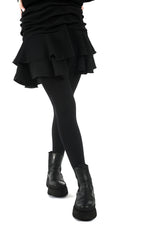 Fustă scurtă neagră cu falduri și jupă pantalon, vedere frontală, purtată cu dresuri și încălțăminte casual.