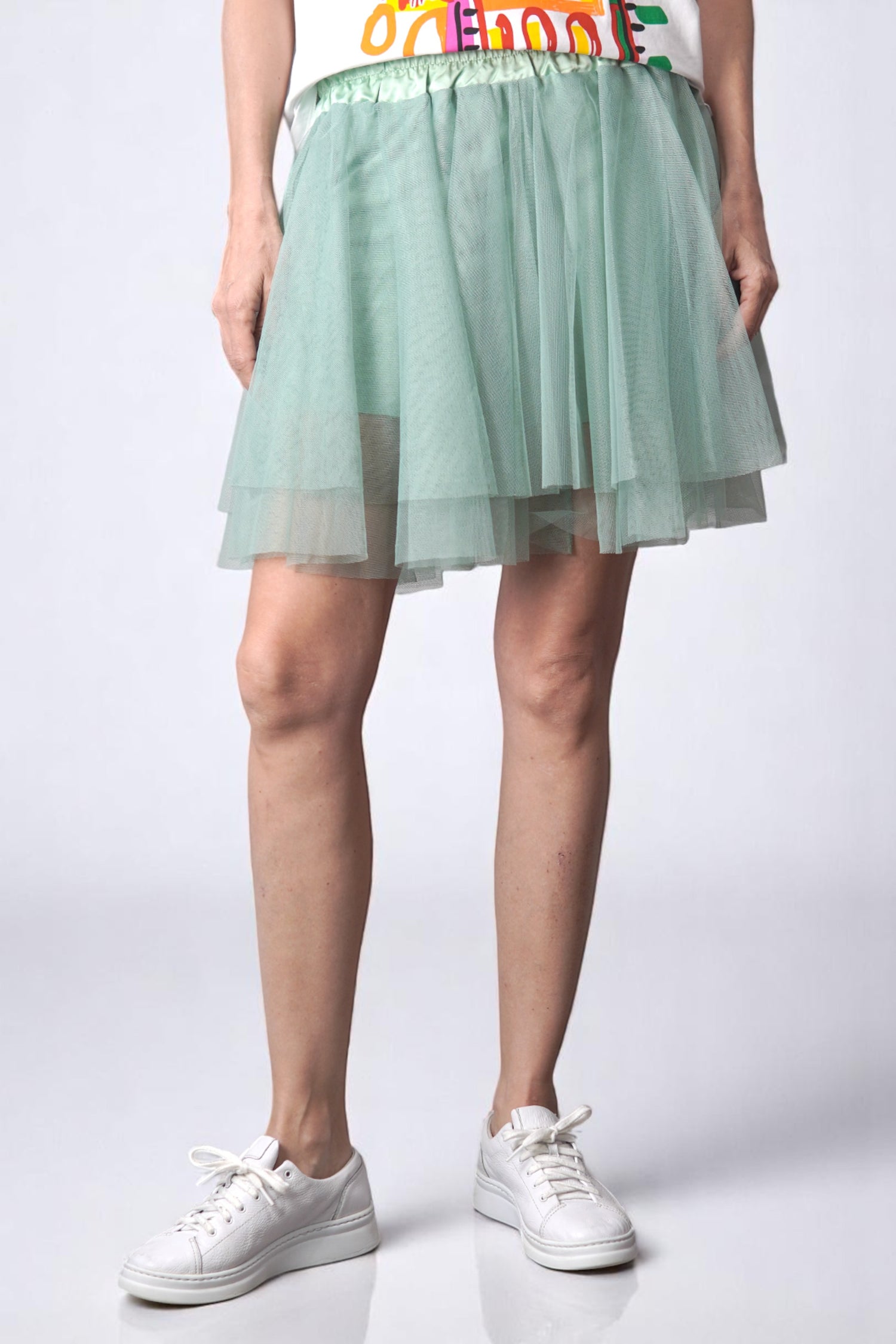 Fustă scurtă din tul verde deschis, cu croială evazată și talie elastică, purtată casual cu pantofi sport.