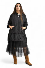 Geacă neagră vaporoasă cu glugă, fermoar și buzunare, din material ușor, prezentată într-un look complet.