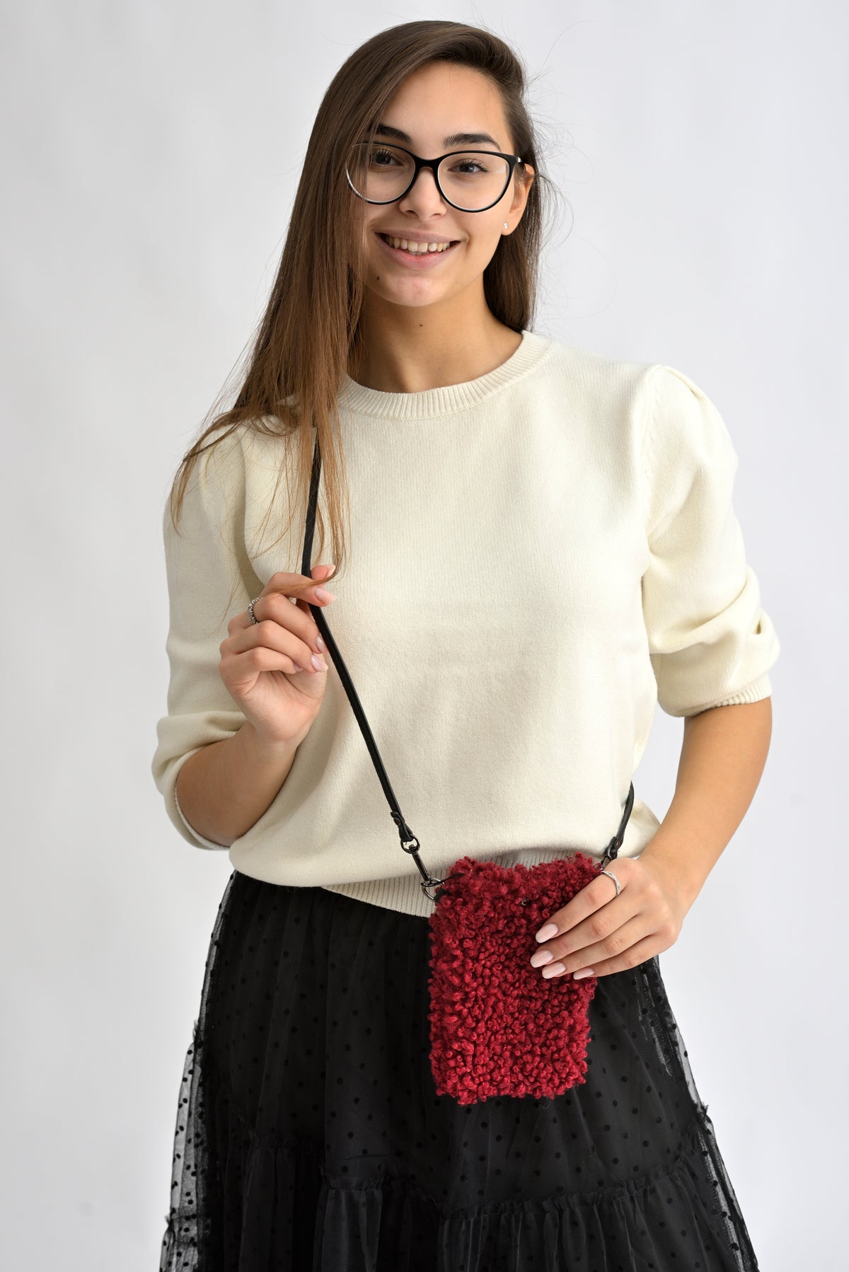 Femeie purtând o geantă mică crossbody pentru telefon, din material bouclé roșu.