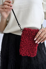 Geantă mică roșie pentru telefon, din material textil bouclé, purtată crossbody.