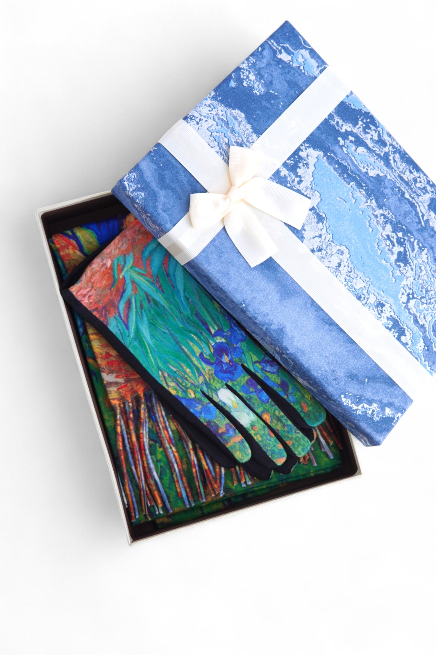 Mănuși colorate cu imprimeu artistic, prezentate într-o cutie cadou albastră cu fundă albă.