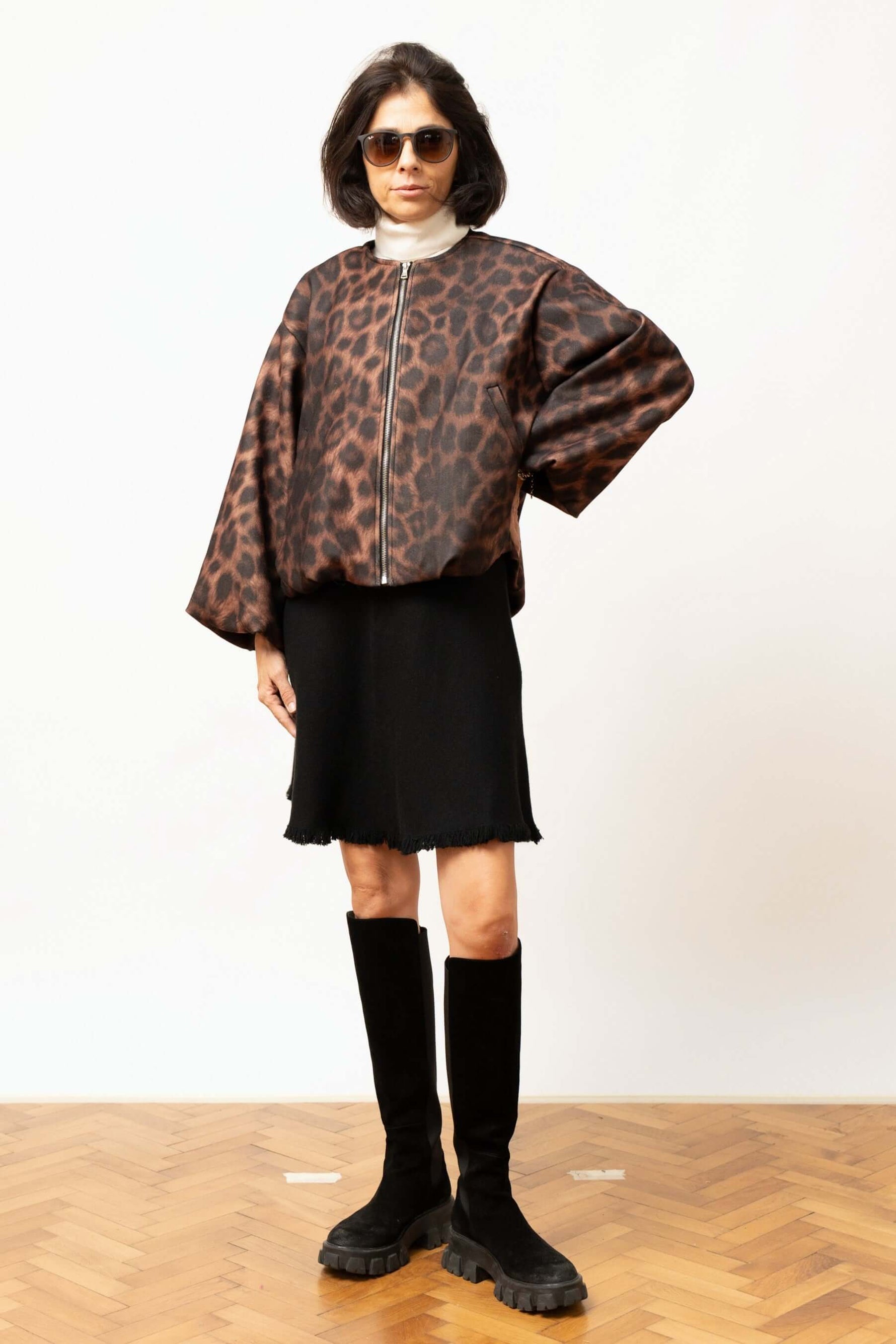 Jachetă cu imprimeu leopard, purtată cu fustă neagră și cizme înalte, aspect modern.