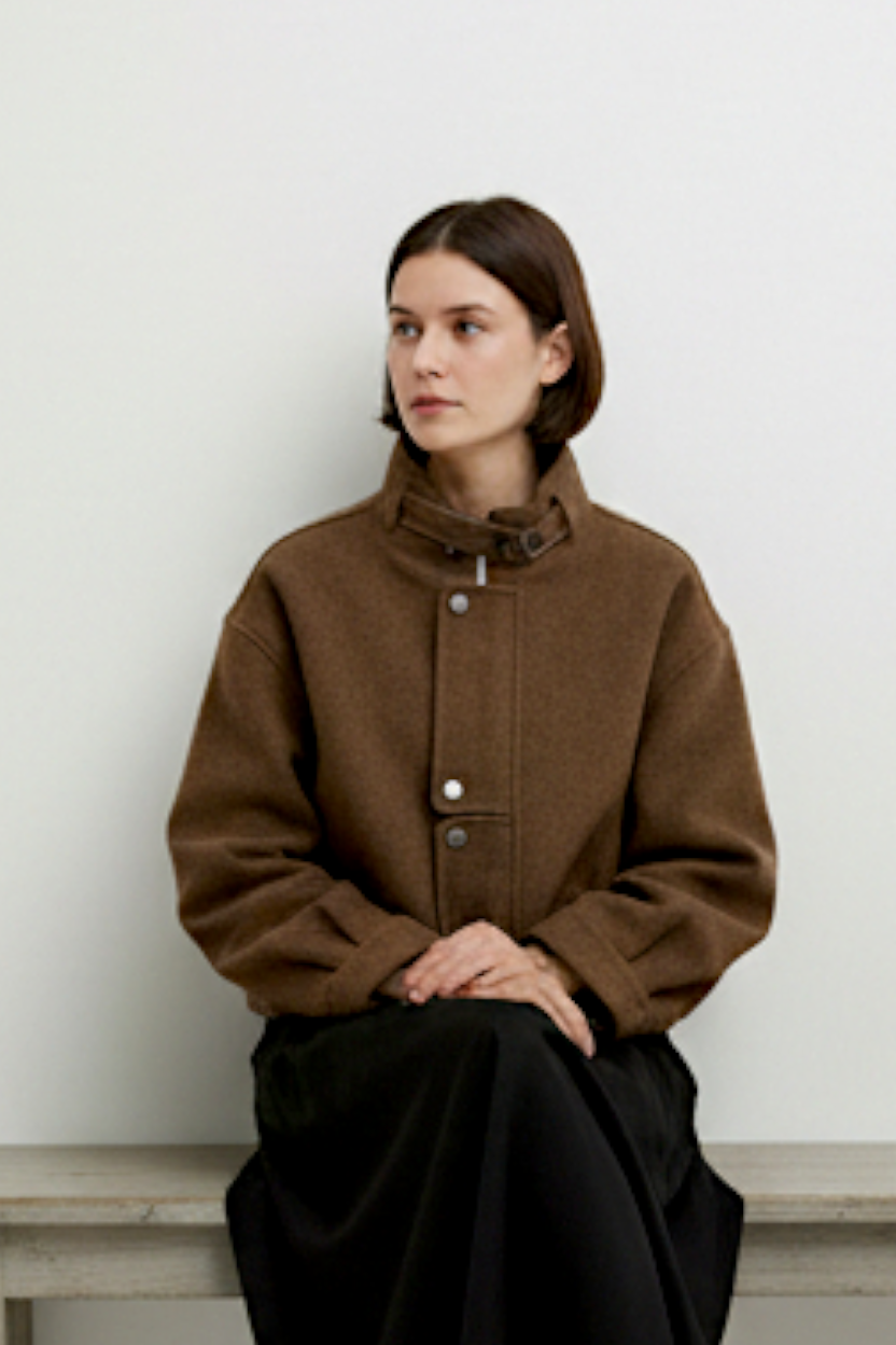 Jachetă scurtă maro cu guler înalt, purtată cu fustă midi și sneakers, ținută urbană de zi.
