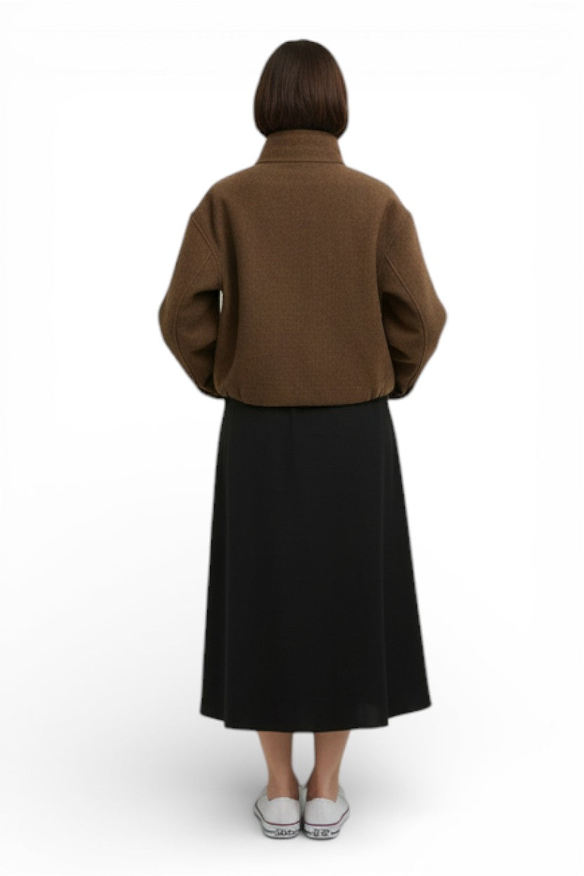 Jachetă scurtă maro, vedere din spate, croială boxy și guler înalt, purtată cu fustă midi neagră.
