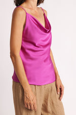 Maiou roz fucsia din satin cu decolteu drapat și bretele subțiri, purtat lejer cu pantaloni din in bej.