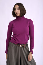 Maletă mov cu guler înalt și nasturi aurii pe manșete, din material moale și elastic, purtată de model.