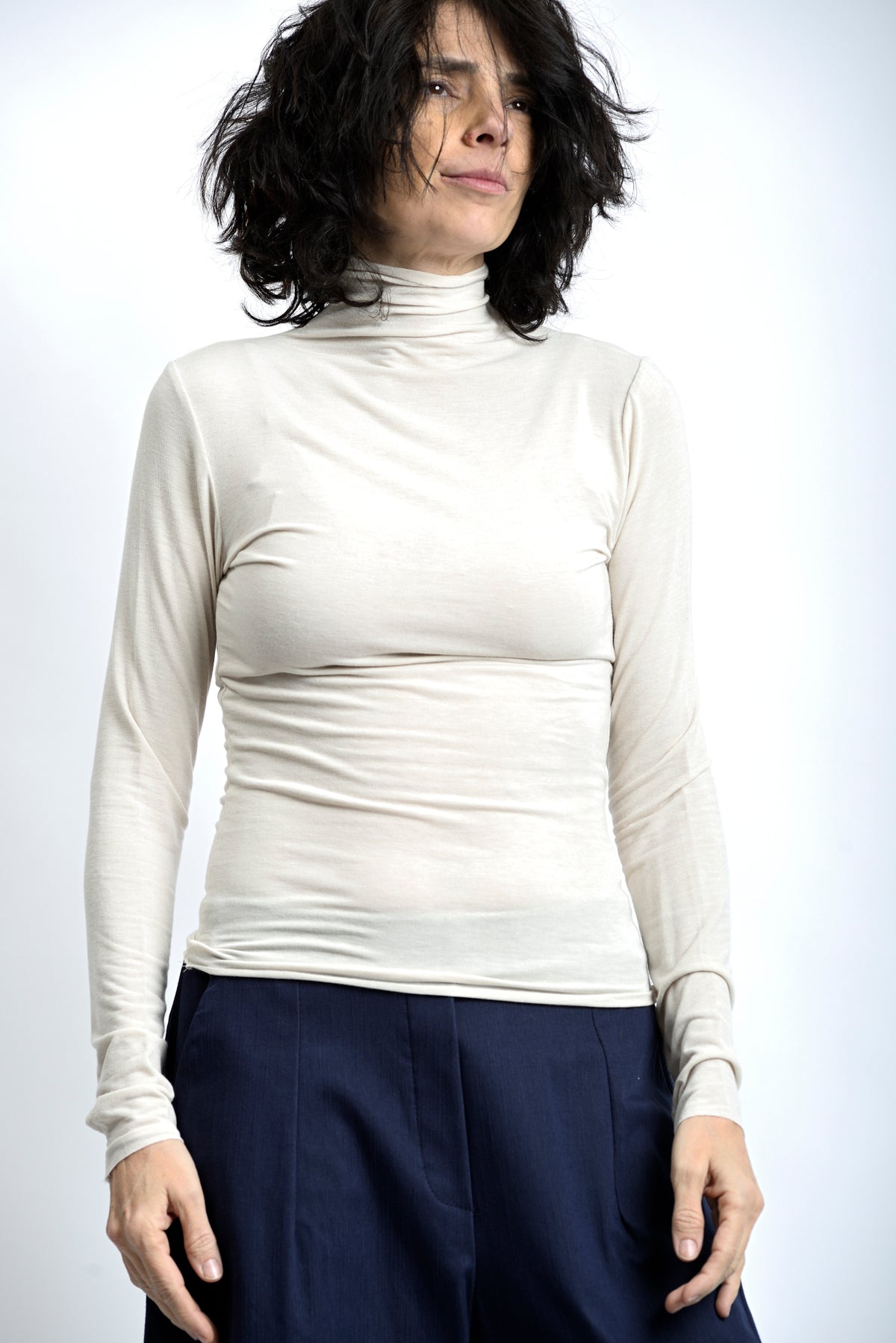 Maletă subțire crem, cu guler înalt și decupaj pentru deget, purtată ca strat de bază.