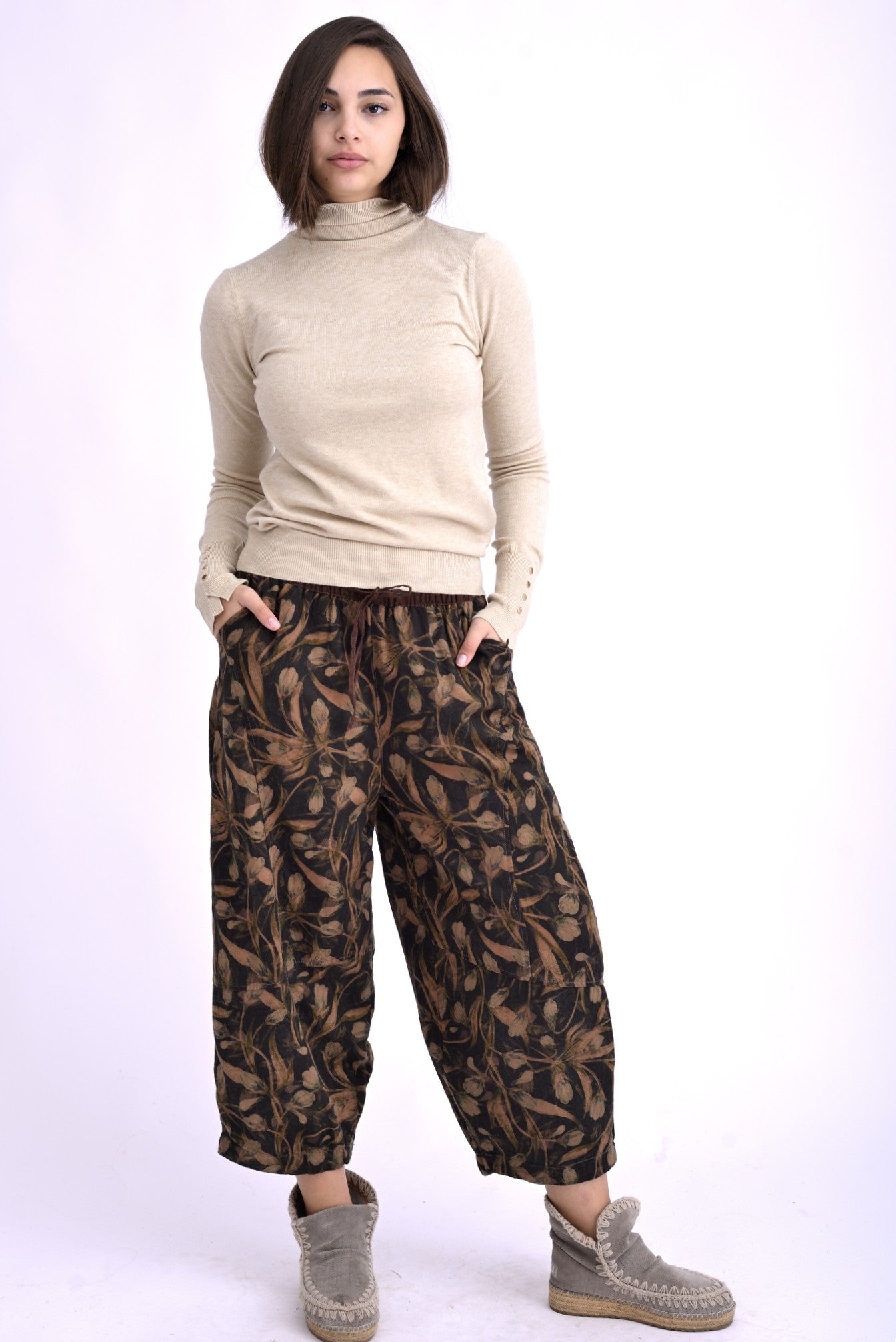 Pantaloni barrel din bumbac 100%, cu imprimeu floral în nuanțe naturale, purtați de model cu maletă bej.