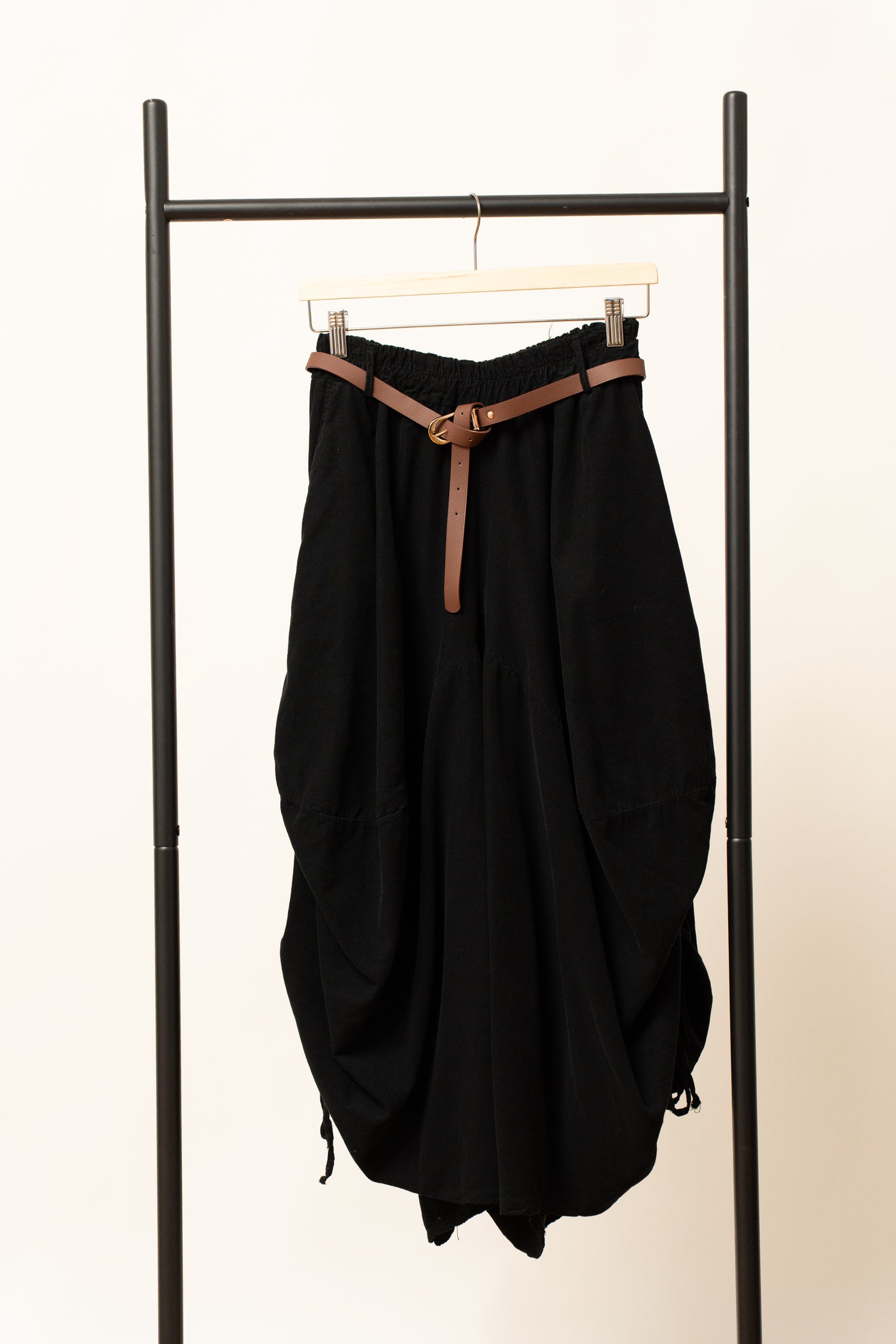 Pantaloni barrel negri, cu croială amplă și curea decorativă, prezentați pe umeraș.