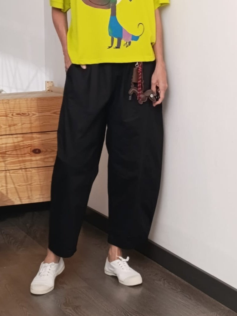 Pantaloni negri tip barrel, din bumbac cu breloc maro, purtați cu tricou galben

