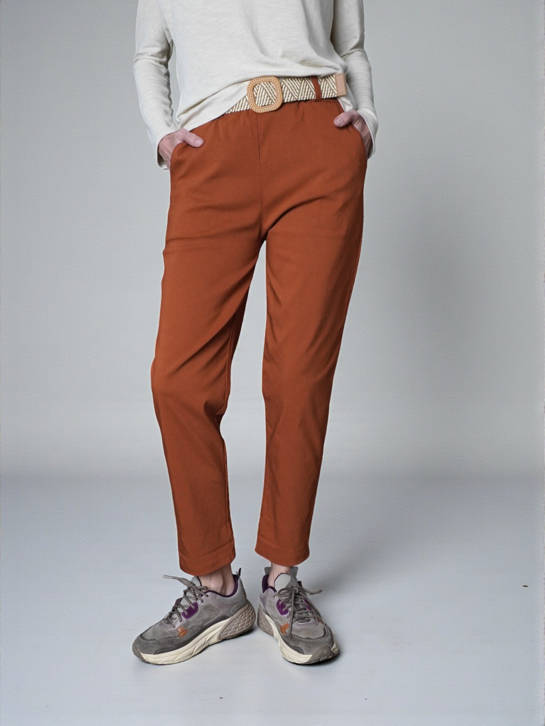 Pantaloni conici culoare cărămiziu, talie elastică, purtați cu pantofi sport, vedere frontală.