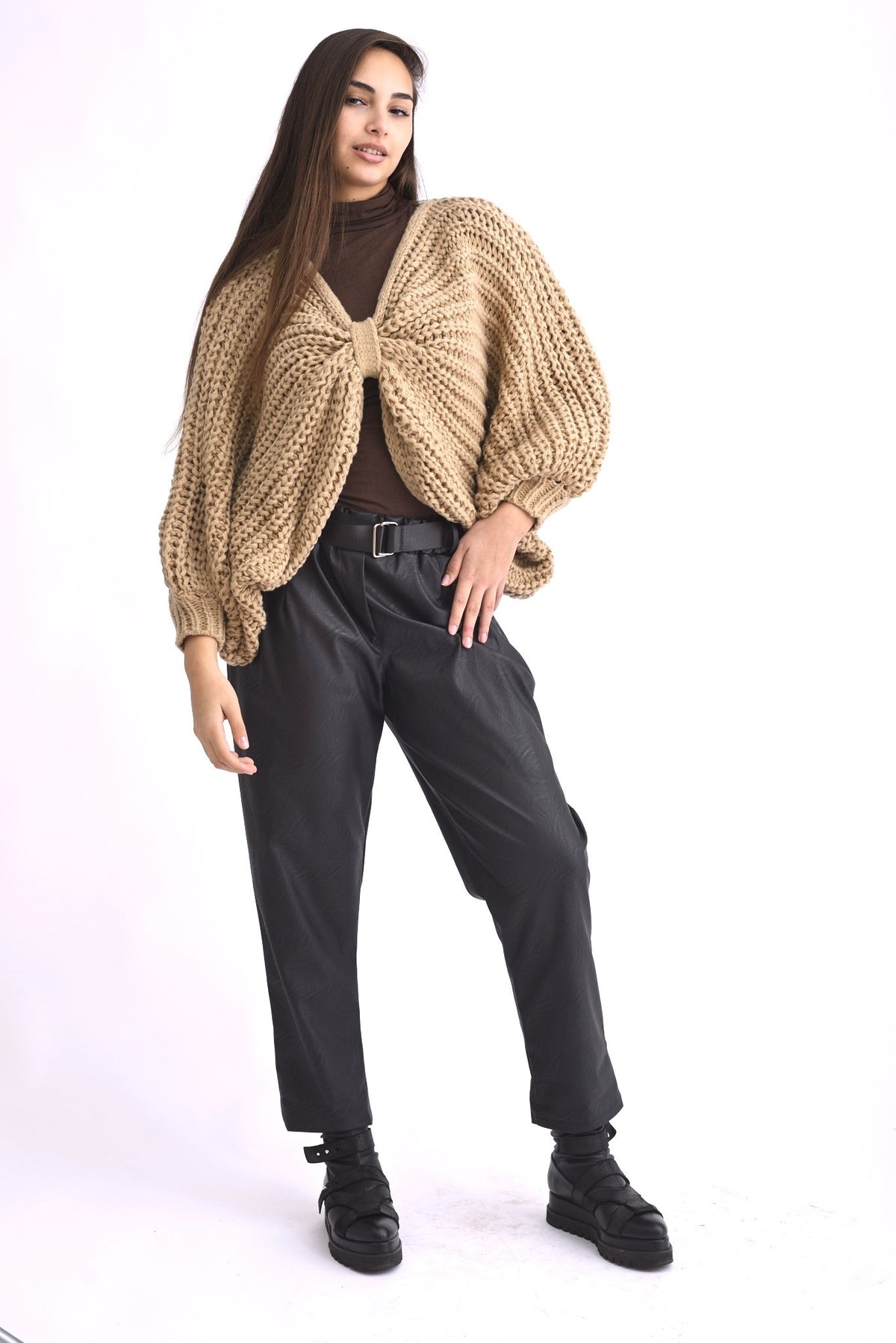 Pantaloni conici din piele ecologică neagră, cu talie elastică și croială lejeră, purtați cu pulover bej.