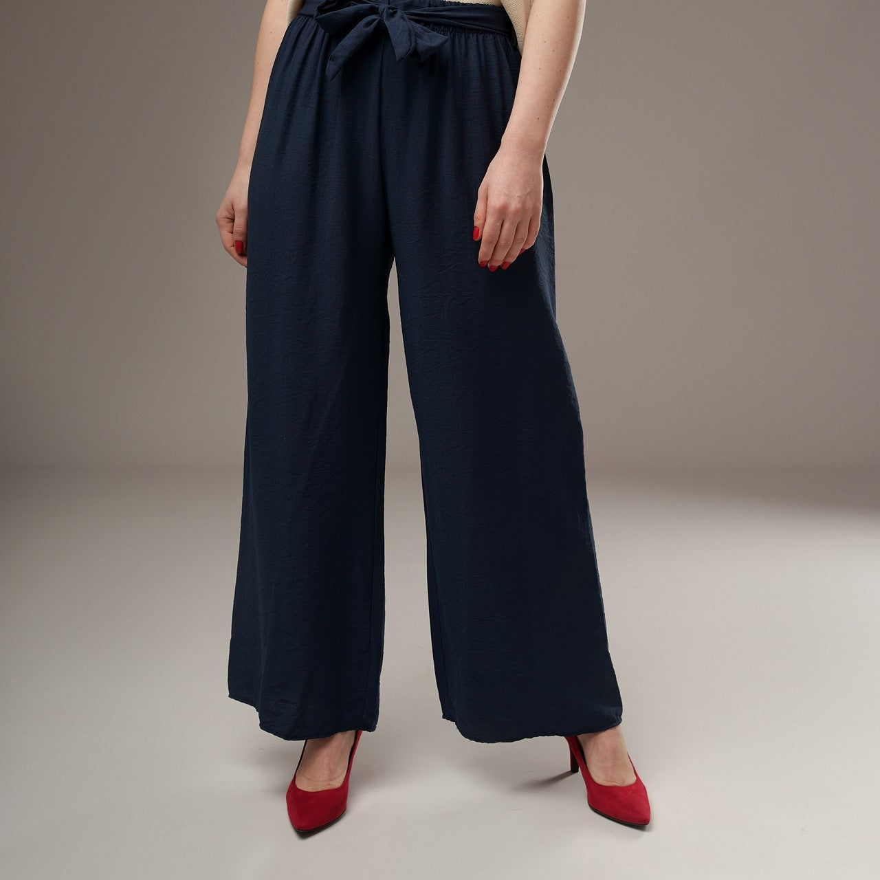Pantaloni evazați bleumarin din viscoză, croială lejeră, purtați cu pantofi roșii, accent pe fluiditatea materialului.